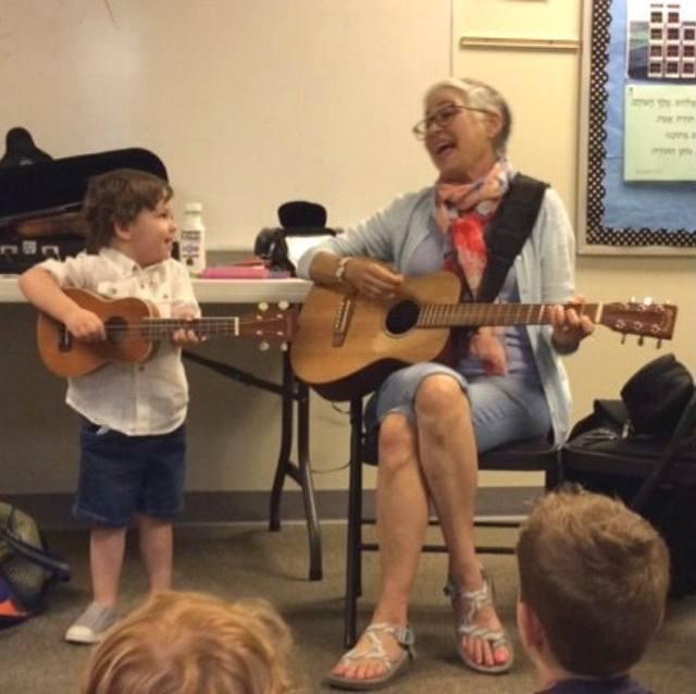 Lisa with the Micah Children's Academy toddlers. She is playing her guitar along with a toddler playing a very tiny guitar